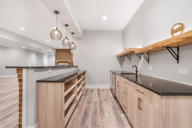 kitchen with light wood-type flooring, kitchen peninsula, sink, decorative light fixtures, and stainless steel dishwasher