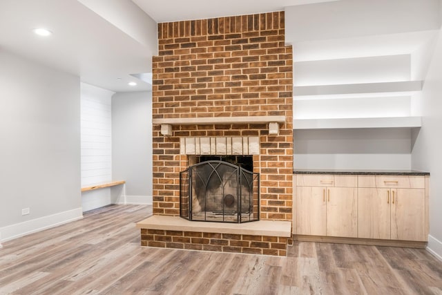 unfurnished living room featuring light wood-type flooring, a brick fireplace, and built in features