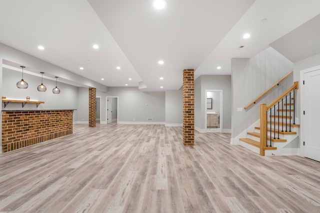 unfurnished living room with ornate columns, bar, and light wood-type flooring