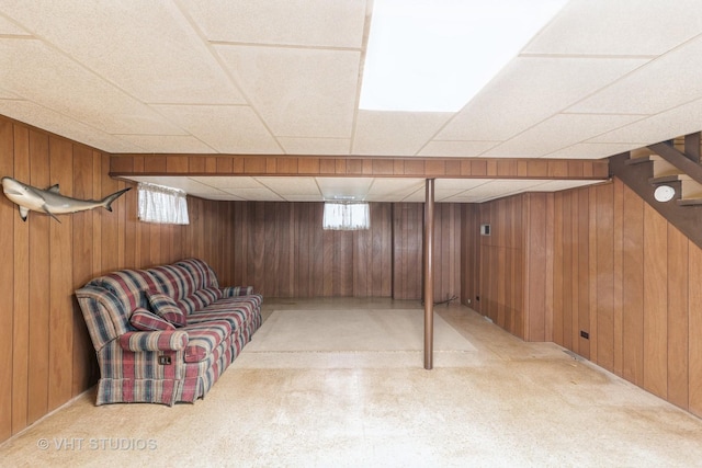 basement with a paneled ceiling, light colored carpet, and wood walls