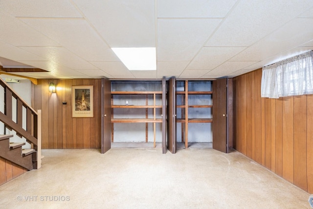 basement featuring a drop ceiling, wooden walls, and carpet flooring