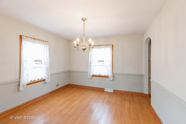 unfurnished room with a notable chandelier, a wealth of natural light, and wood-type flooring