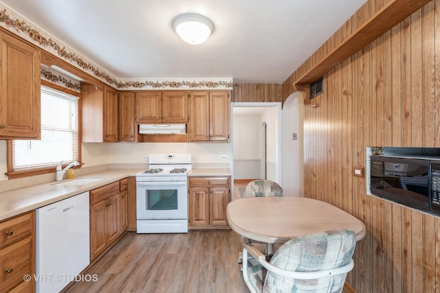 kitchen with sink, white appliances, wooden walls, and light wood-type flooring