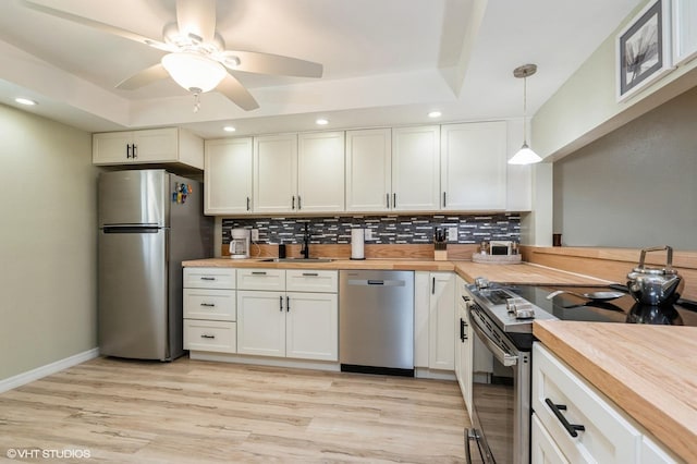 kitchen with stainless steel appliances, a tray ceiling, ceiling fan, white cabinets, and hanging light fixtures