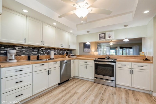 kitchen with butcher block counters, sink, hanging light fixtures, stainless steel appliances, and white cabinets