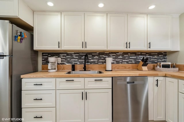 kitchen with decorative backsplash, stainless steel appliances, sink, butcher block countertops, and white cabinetry