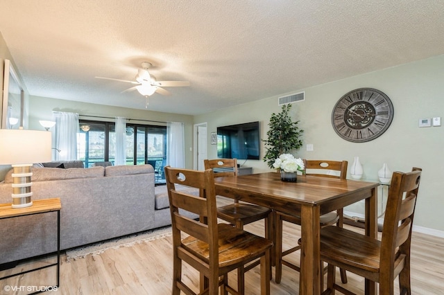 dining room featuring ceiling fan, light wood-type flooring, and a textured ceiling