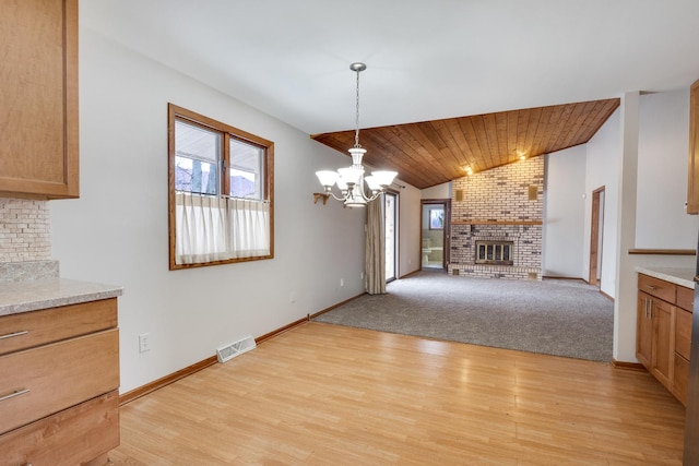 unfurnished dining area featuring a brick fireplace, light hardwood / wood-style flooring, lofted ceiling, and a chandelier