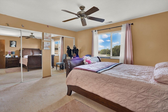 bedroom featuring ceiling fan, light carpet, and multiple closets