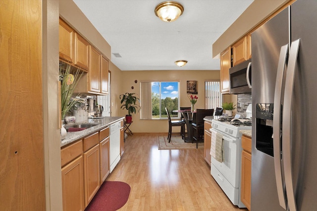 kitchen featuring light stone countertops, appliances with stainless steel finishes, tasteful backsplash, sink, and light hardwood / wood-style floors