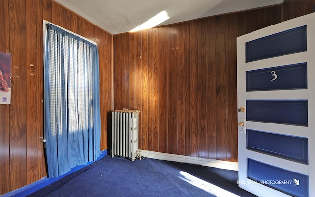 carpeted spare room with radiator and wood walls