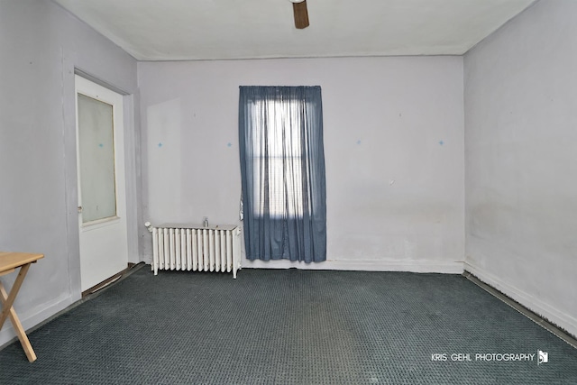 carpeted empty room with ceiling fan and radiator