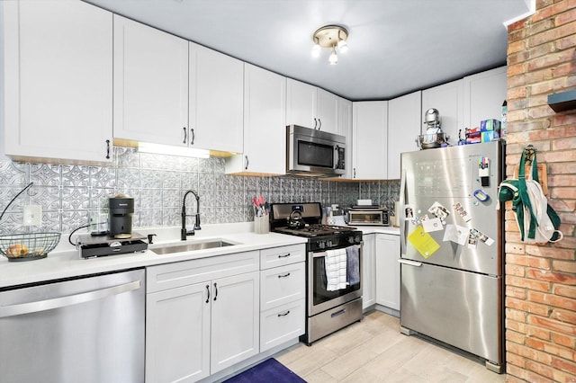 kitchen with brick wall, tasteful backsplash, white cabinetry, sink, and stainless steel appliances