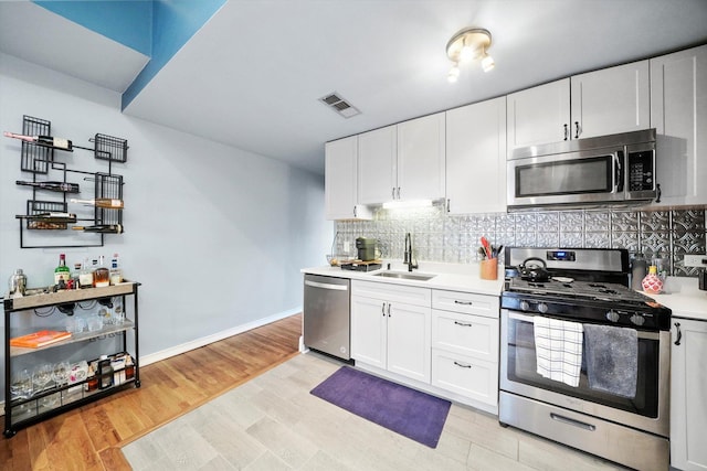 kitchen featuring sink, white cabinets, backsplash, light hardwood / wood-style floors, and stainless steel appliances