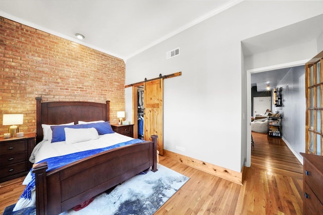 bedroom with hardwood / wood-style flooring, brick wall, a barn door, and crown molding