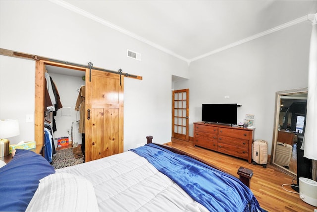 bedroom with wood-type flooring, ornamental molding, and a barn door