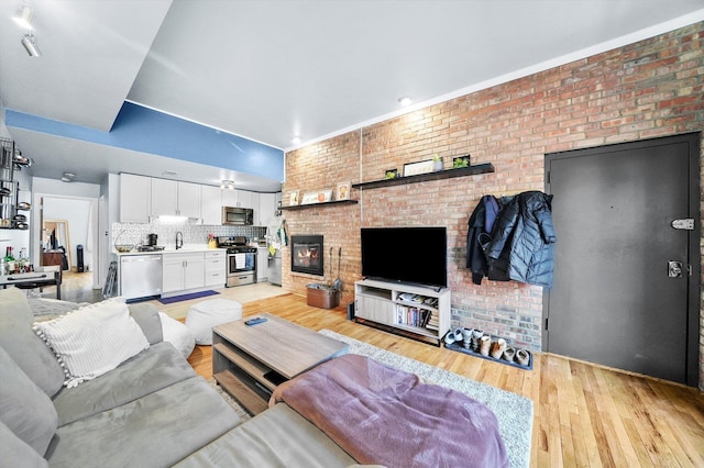 living room featuring brick wall, sink, and light hardwood / wood-style floors