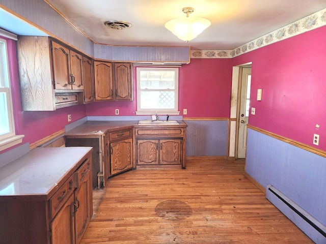 kitchen with light wood-style floors, a sink, a baseboard heating unit, and brown cabinets