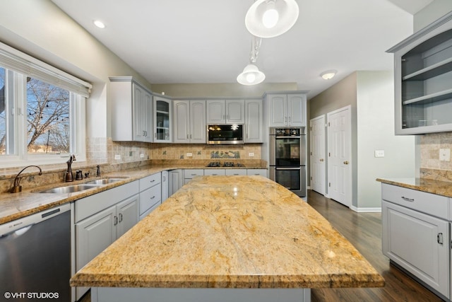 kitchen with appliances with stainless steel finishes, backsplash, light stone counters, decorative light fixtures, and a center island