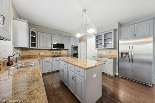 kitchen with hanging light fixtures, sink, light stone countertops, appliances with stainless steel finishes, and a kitchen island