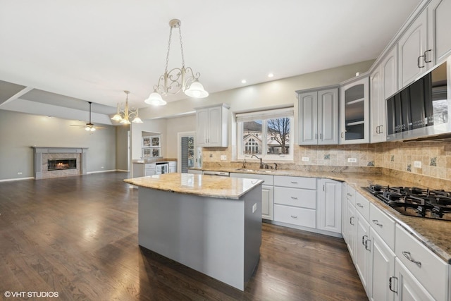 kitchen with ceiling fan with notable chandelier, gas stovetop, sink, decorative light fixtures, and a kitchen island