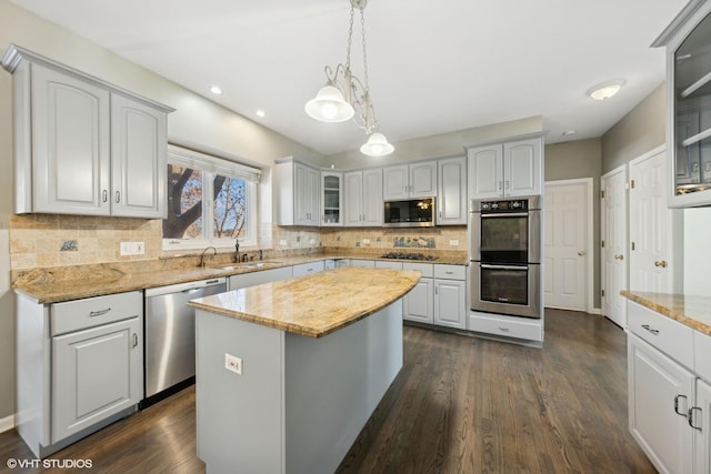 kitchen featuring light stone countertops, stainless steel appliances, sink, decorative light fixtures, and a kitchen island