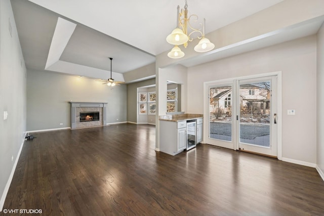 unfurnished living room with dark wood-type flooring, a raised ceiling, wine cooler, a high end fireplace, and ceiling fan with notable chandelier