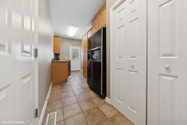 kitchen with light brown cabinetry and black refrigerator with ice dispenser