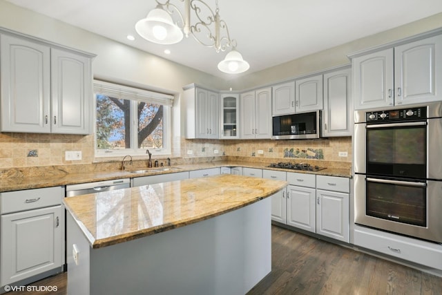 kitchen with light stone countertops, stainless steel appliances, sink, decorative light fixtures, and a kitchen island