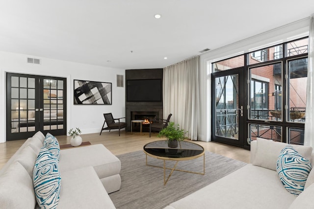 living room featuring a large fireplace, light hardwood / wood-style floors, and french doors