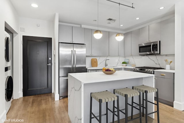 kitchen with stacked washer and dryer, gray cabinets, a breakfast bar area, hanging light fixtures, and stainless steel appliances