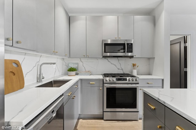 kitchen featuring sink, light stone counters, tasteful backsplash, gray cabinets, and stainless steel appliances