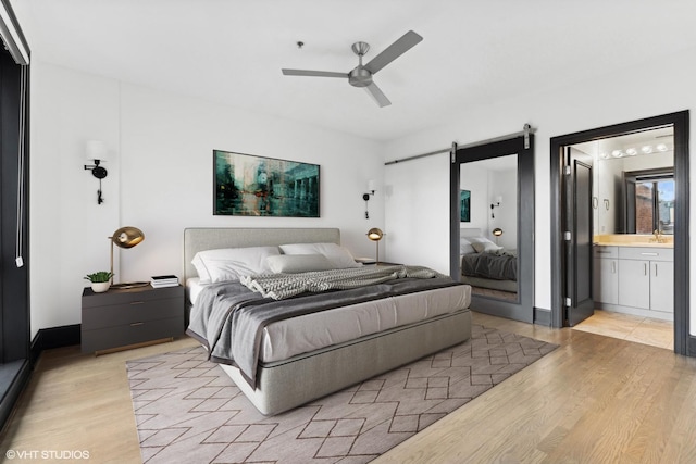 bedroom featuring ceiling fan, a barn door, connected bathroom, and light hardwood / wood-style floors