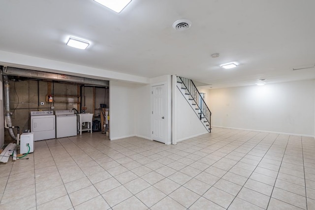 basement featuring washing machine and dryer, sink, and light tile patterned flooring