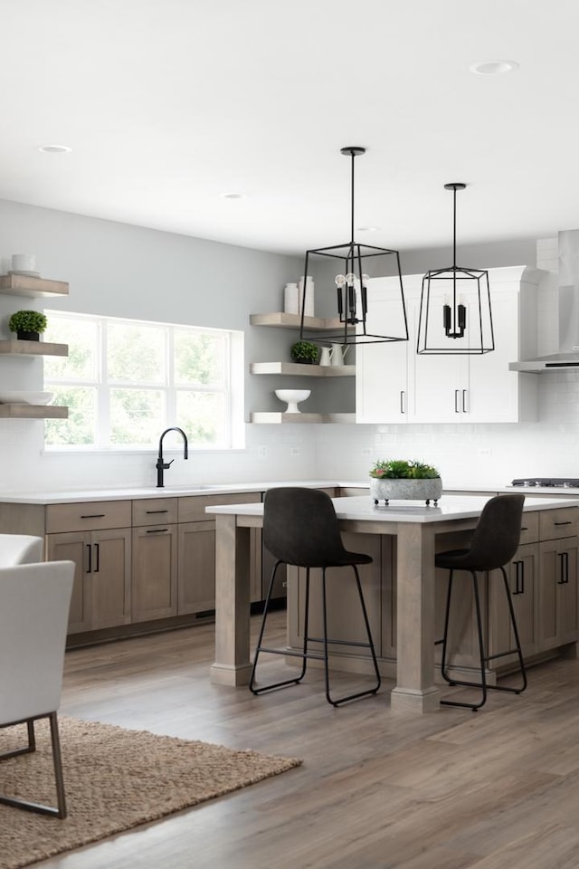 kitchen featuring pendant lighting, wall chimney exhaust hood, light wood-type flooring, tasteful backsplash, and a breakfast bar