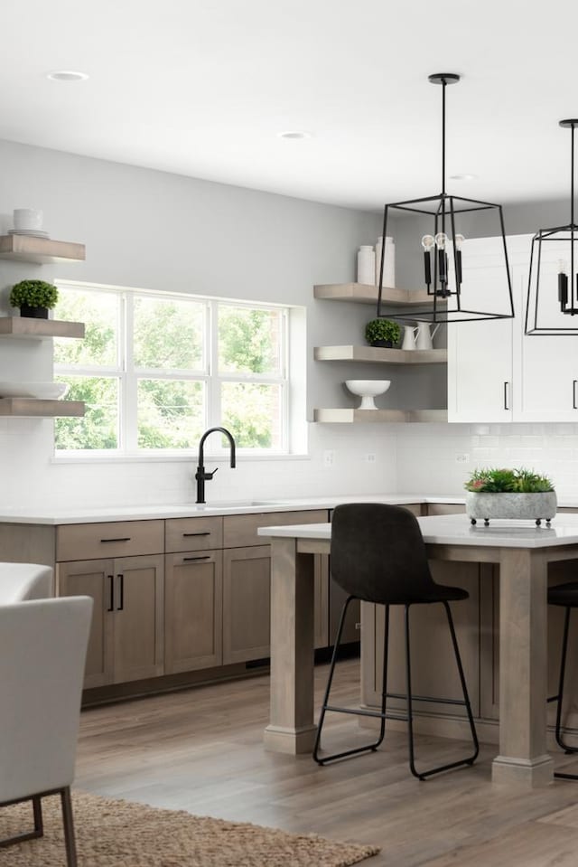 kitchen featuring decorative light fixtures, tasteful backsplash, sink, light wood-type flooring, and a breakfast bar area