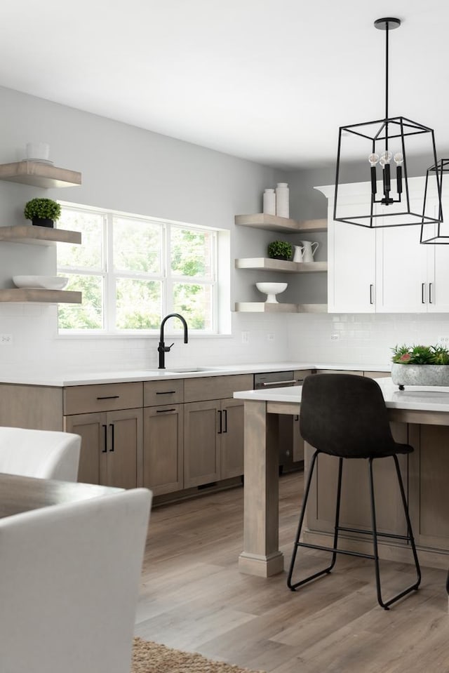 kitchen with tasteful backsplash, hanging light fixtures, sink, light hardwood / wood-style flooring, and a breakfast bar area