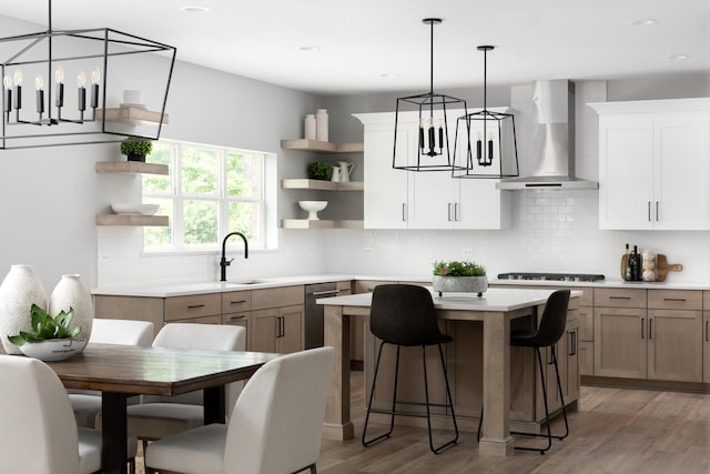 kitchen featuring a center island, wall chimney exhaust hood, wood-type flooring, white cabinetry, and sink