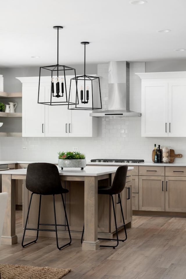 kitchen with wall chimney exhaust hood, a kitchen island, decorative light fixtures, white cabinetry, and light hardwood / wood-style floors