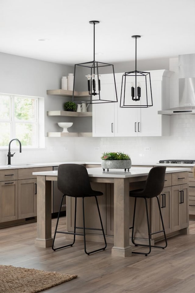 kitchen with wall chimney range hood, light hardwood / wood-style flooring, and hanging light fixtures