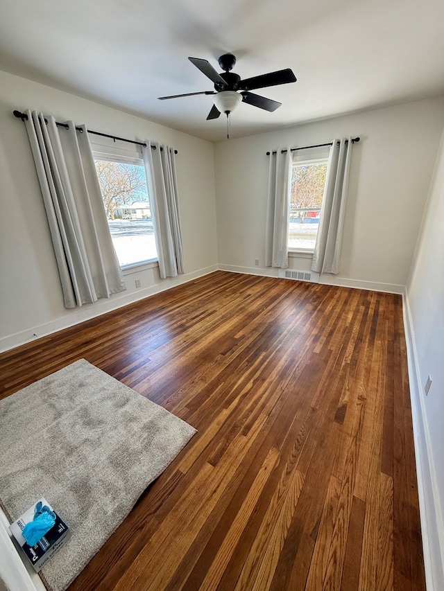 empty room with ceiling fan, a wealth of natural light, and dark hardwood / wood-style flooring