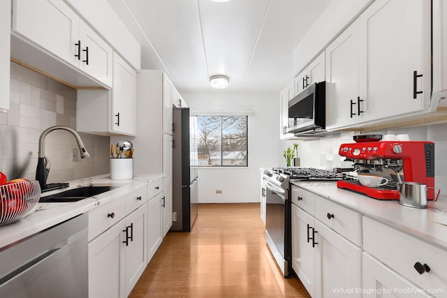 kitchen with light hardwood / wood-style floors, decorative backsplash, sink, white cabinetry, and appliances with stainless steel finishes