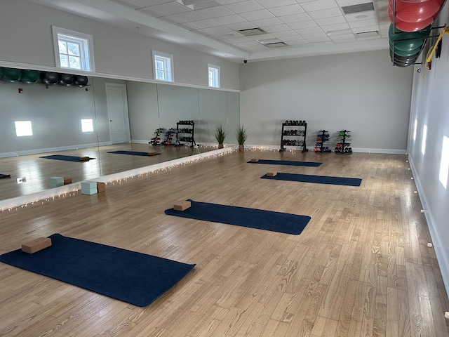 workout area featuring wood-type flooring, visible vents, a towering ceiling, a drop ceiling, and baseboards