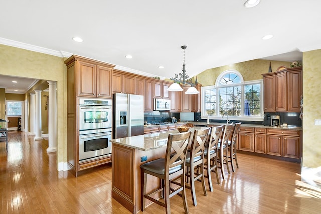 kitchen with appliances with stainless steel finishes, decorative columns, a kitchen breakfast bar, a kitchen island, and decorative light fixtures