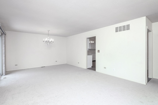 carpeted spare room featuring a textured ceiling and an inviting chandelier