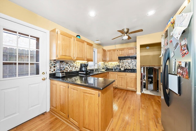 kitchen featuring light wood-type flooring, kitchen peninsula, tasteful backsplash, and stainless steel refrigerator