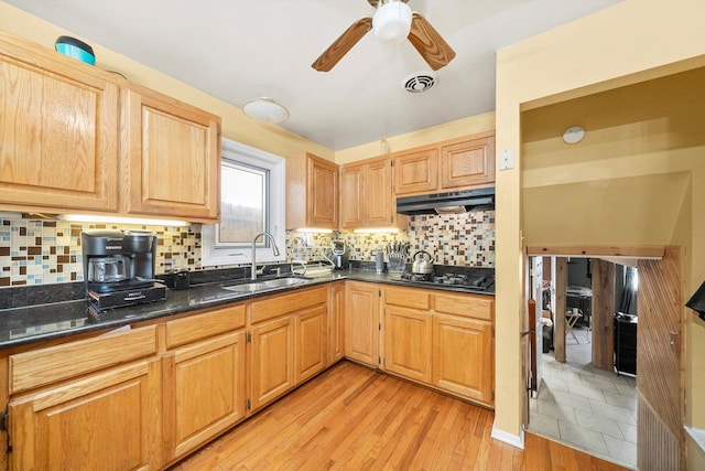 kitchen with black gas stovetop, backsplash, dark stone countertops, sink, and light hardwood / wood-style flooring