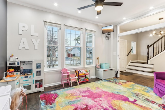 rec room with crown molding, a wealth of natural light, ceiling fan, and dark hardwood / wood-style flooring