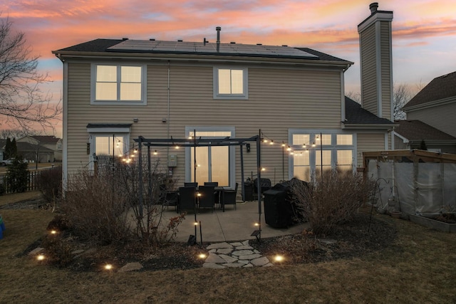 back house at dusk featuring a pergola, a patio, and solar panels