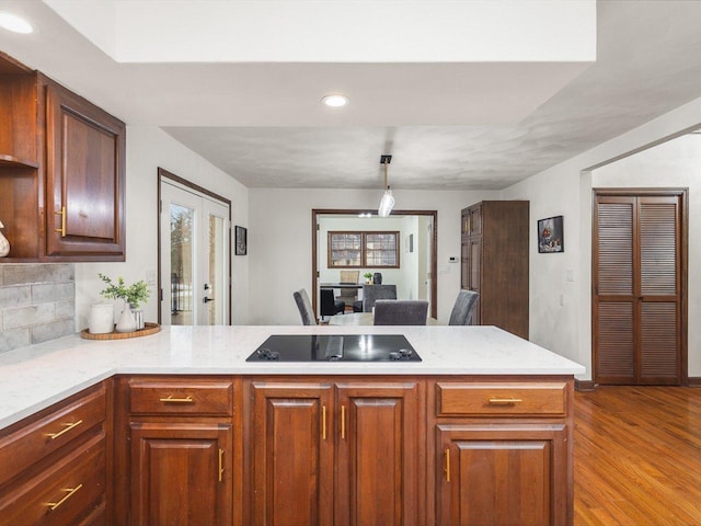 kitchen featuring kitchen peninsula, black electric stovetop, tasteful backsplash, pendant lighting, and light hardwood / wood-style floors